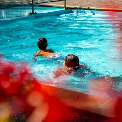 Deux enfants nagent dans une piscine ensoleillée.