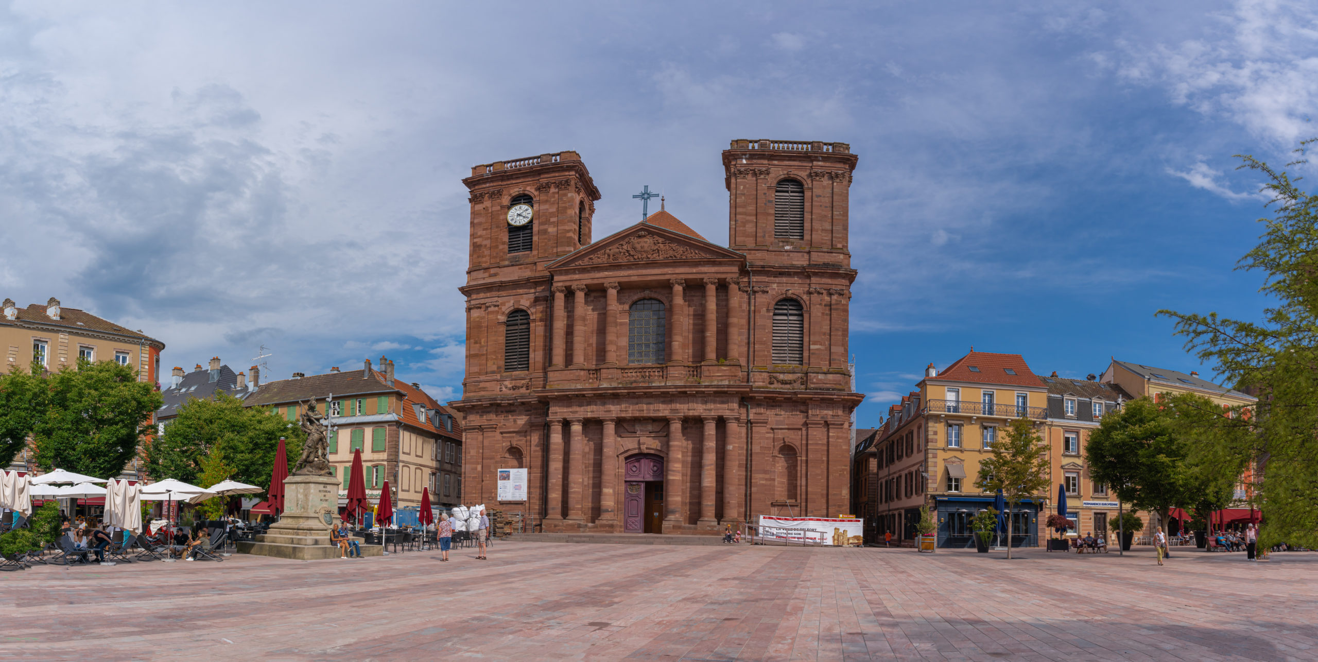 Cathédrale en pierre brun-rouge sous ciel bleu, place centrale.