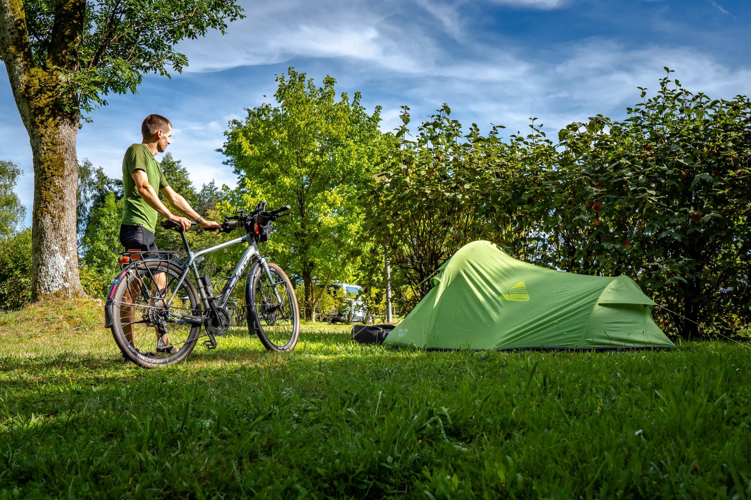 Cycliste et tente verte dans un camping ensoleillé.
