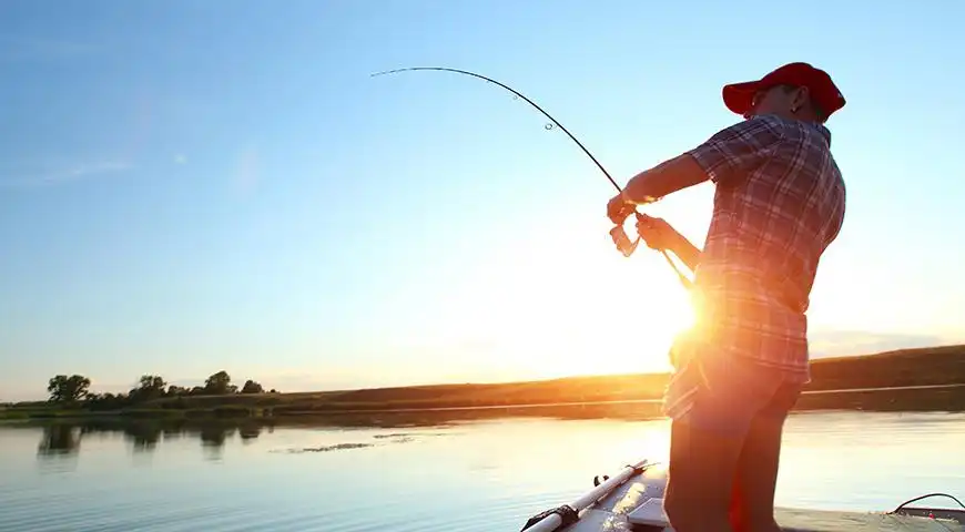 Homme pêche au coucher du soleil sur lac.