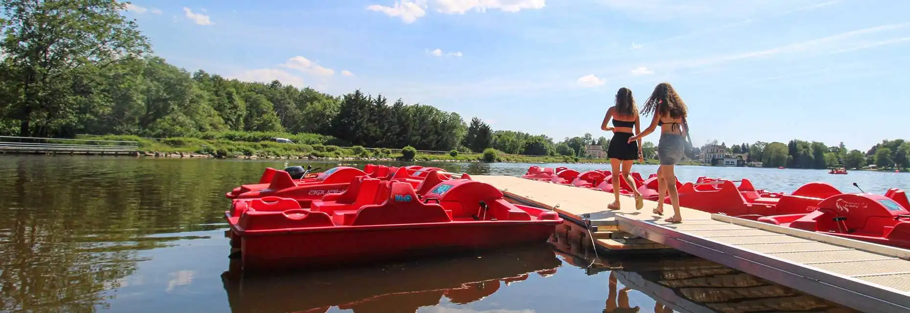 Pédalos rouges sur lac, deux personnes sur le quai.