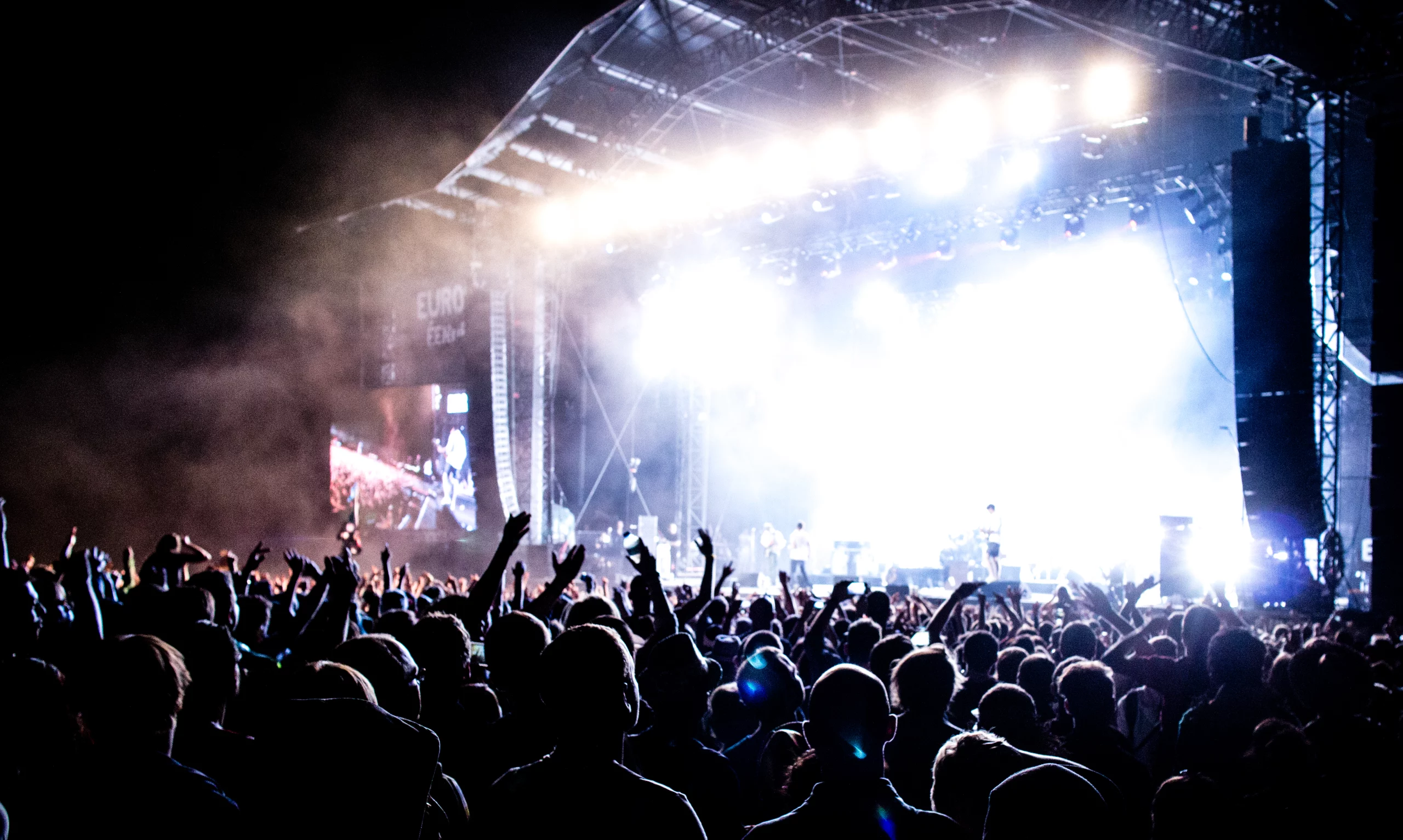 Concert en plein air, foule applaudissant sous les lumières.