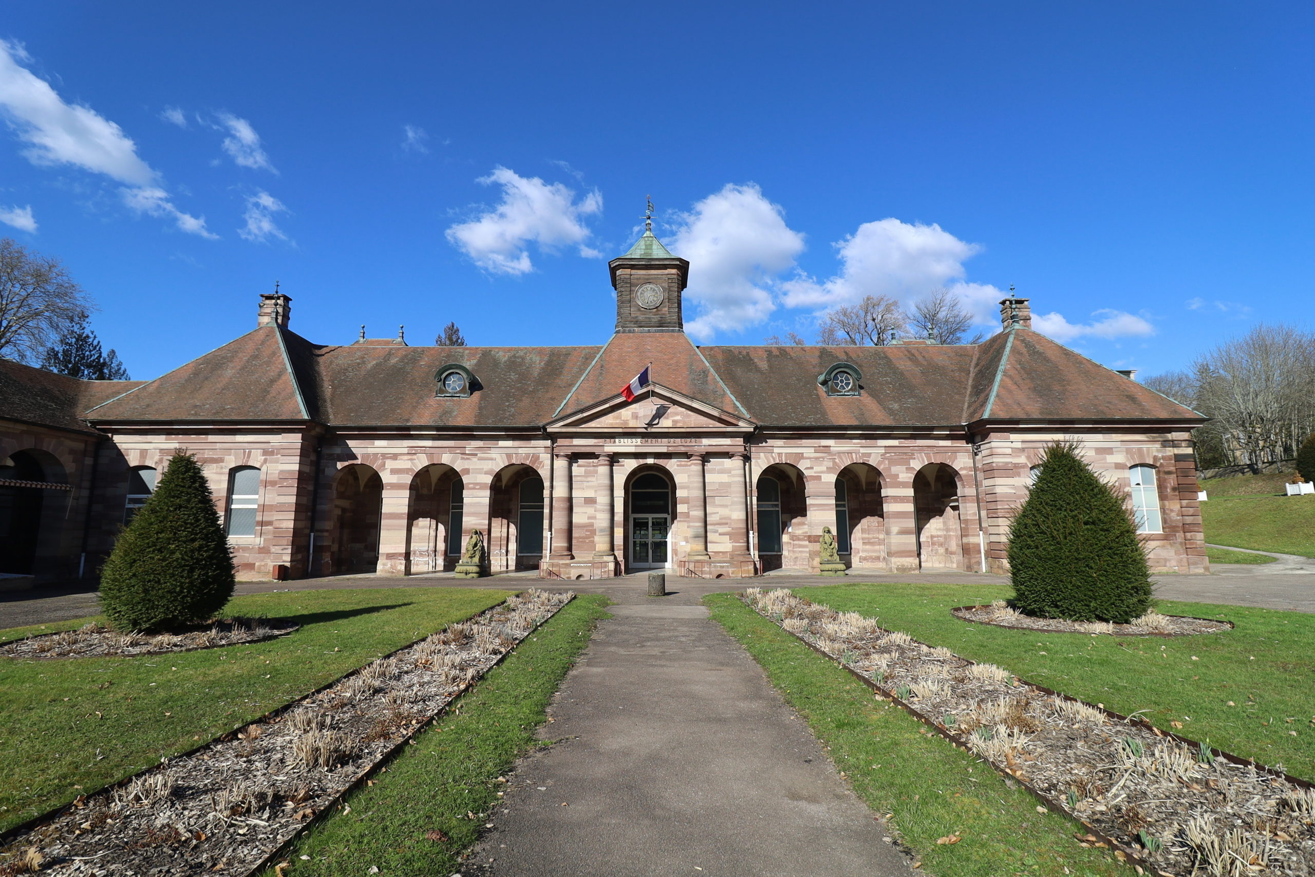 Bâtiment historique avec jardin devant, ciel bleu.