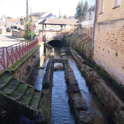 Petit canal urbain avec pont et mur en pierre.