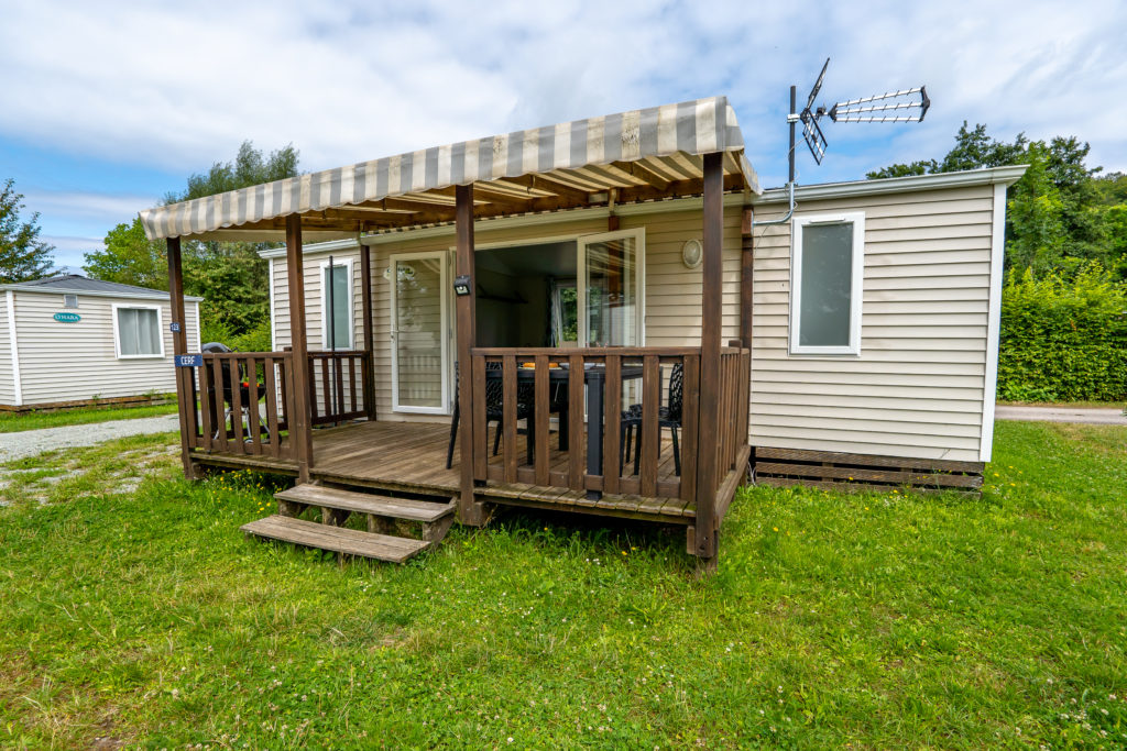 Mobil-home avec terrasse en bois, parc verdoyant.