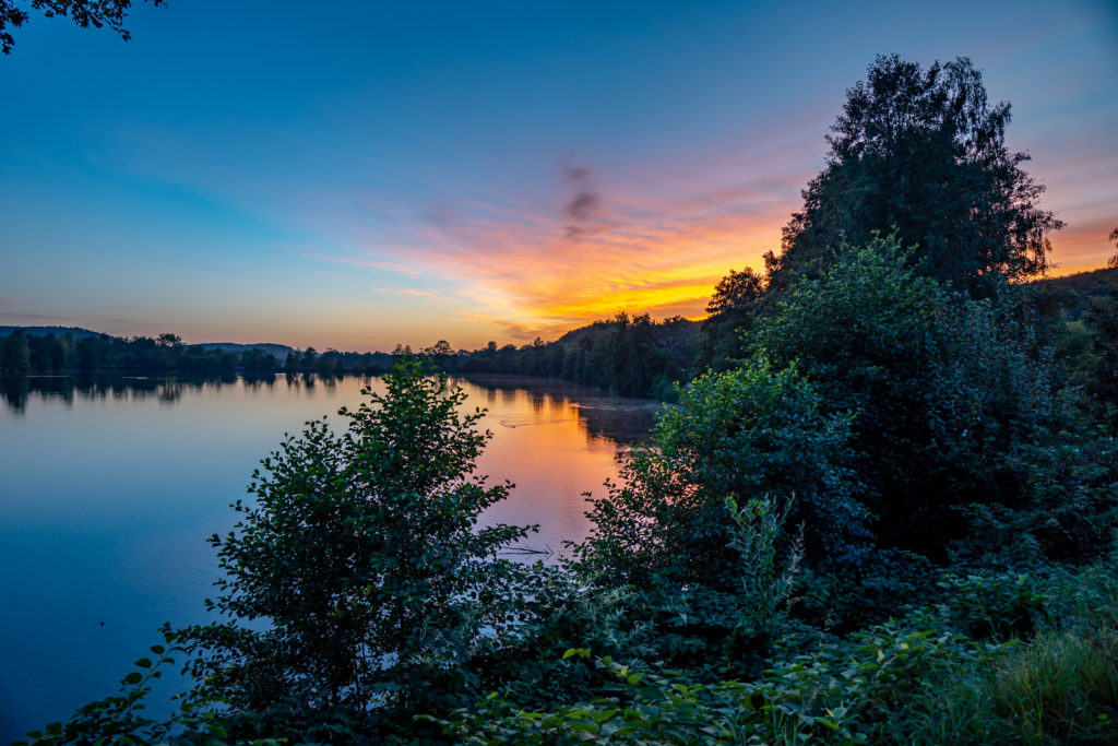Coucher de soleil sur lac paisible et forêt dense.