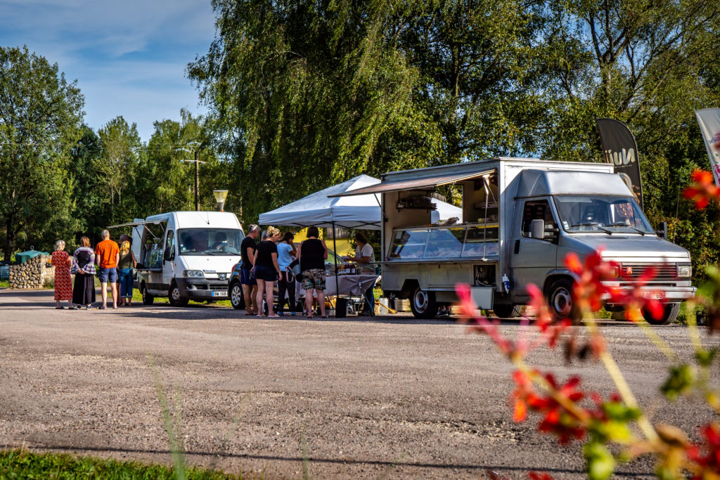Personnes en file devant un food truck sous arbres.