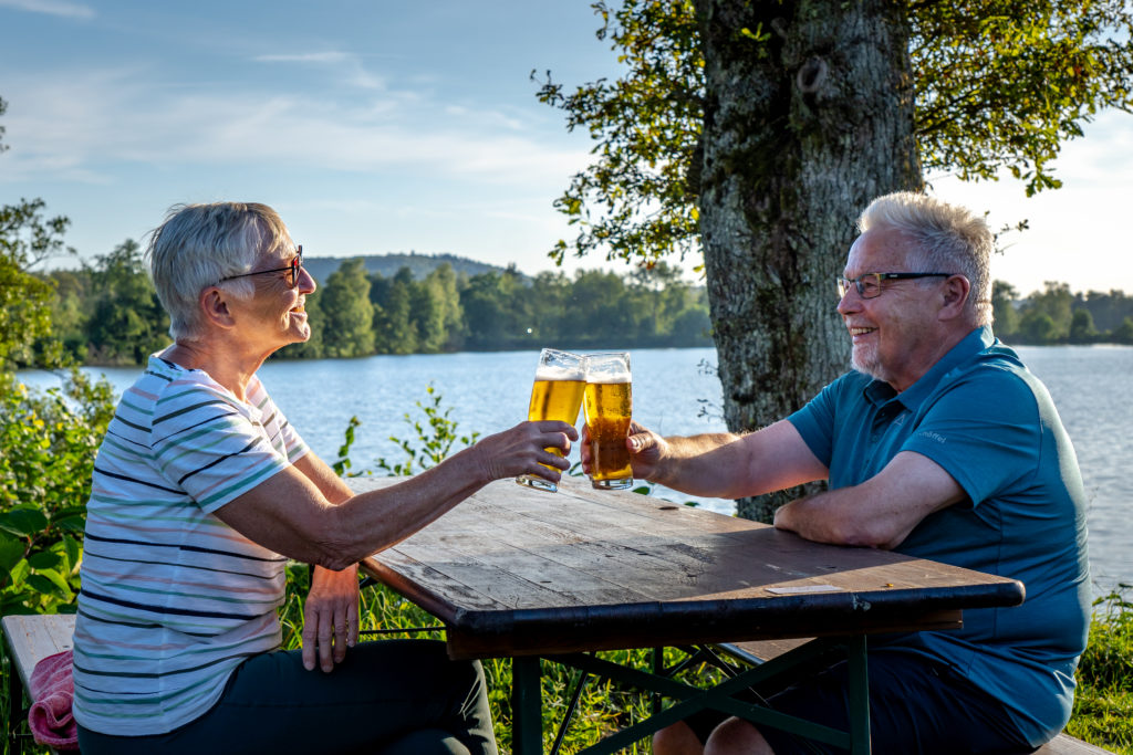 Couple trinquant avec bière au bord d'un lac.