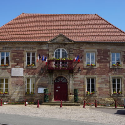 Mairie française en pierre avec drapeaux et voitures.