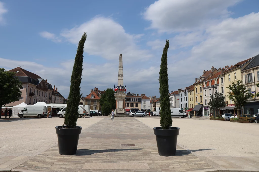 Place avec obélisque, arbres et bâtiments historiques.